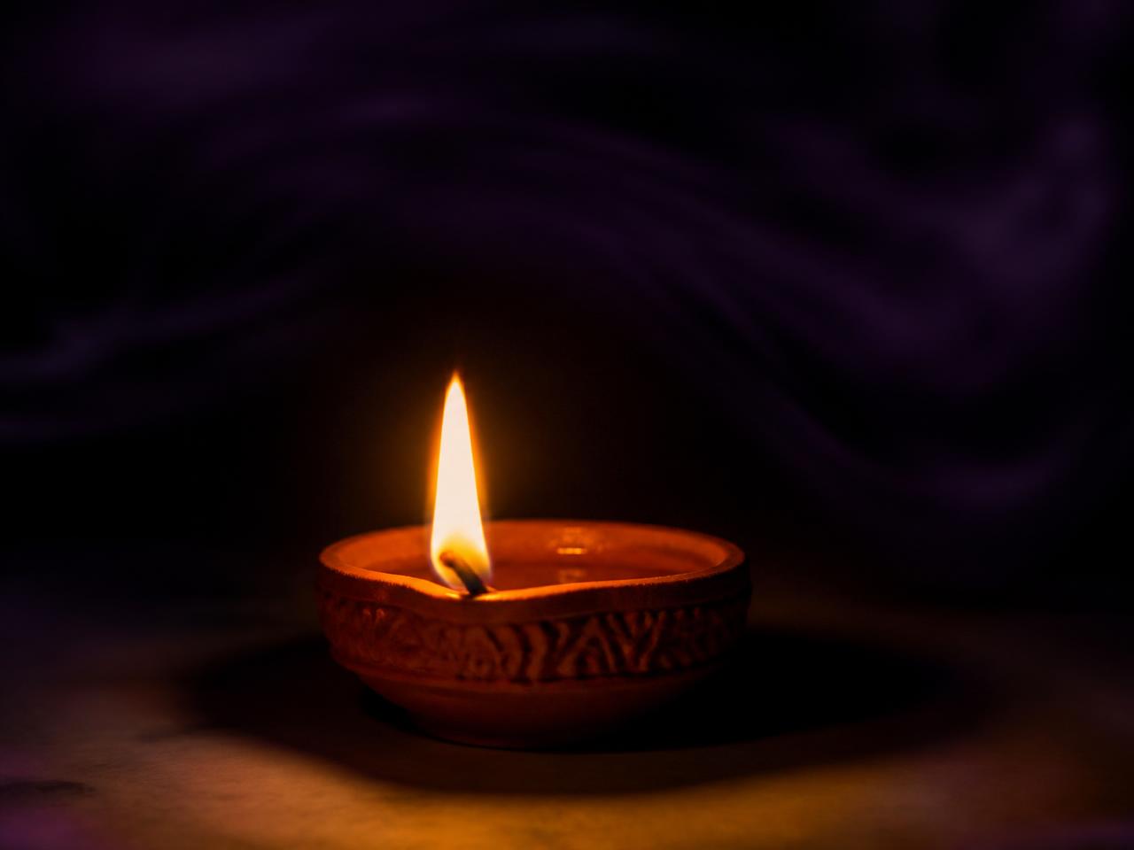 A single lit diya glowing in a dark room
